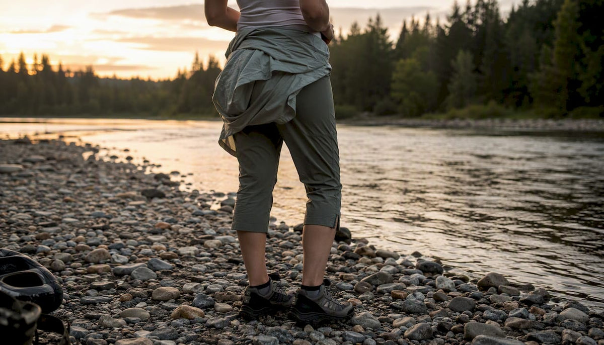 Woman in layered fishing clothes by river at dawn