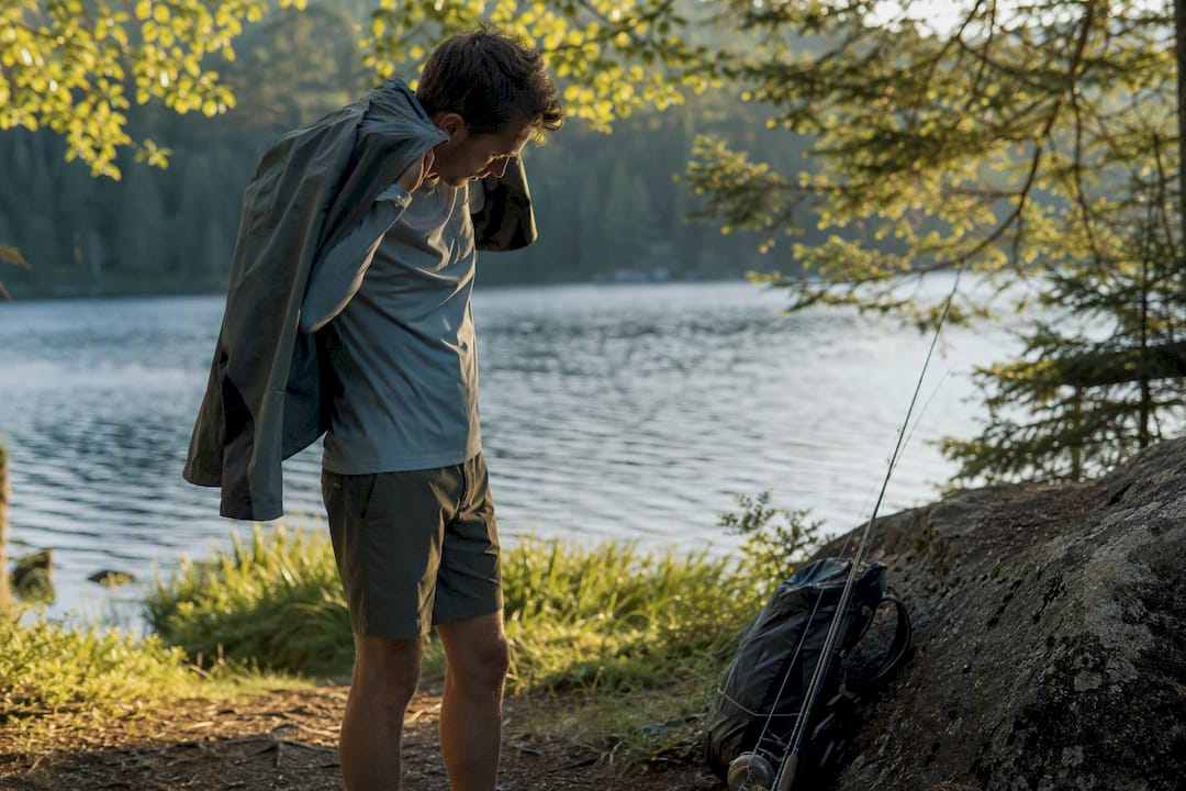 Hiker adjusting layered outfit at forest trailhead dawn
