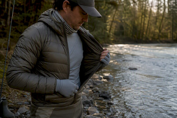 Angler adjusting layered clothes by river at dawn