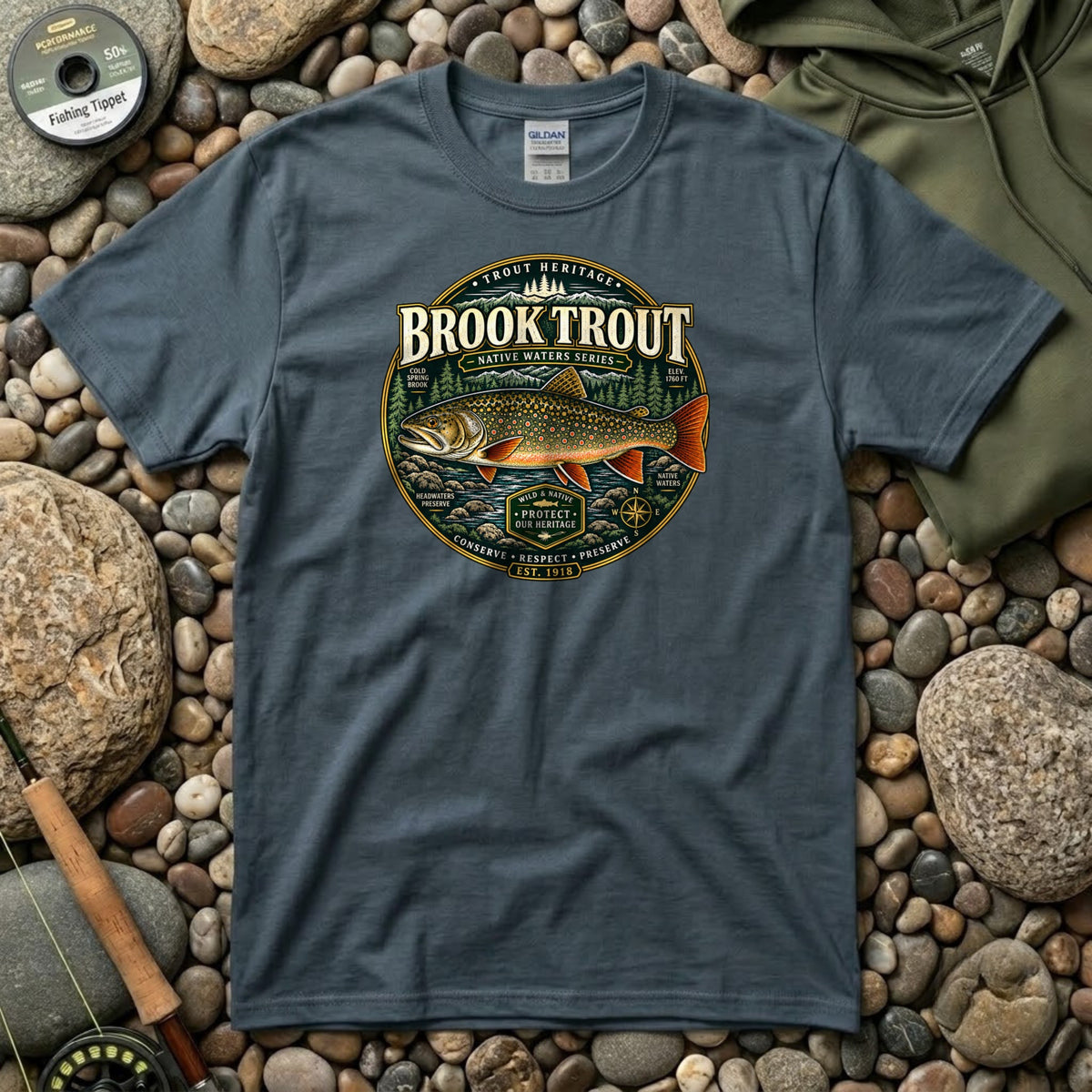 Brook Trout t-shirt in dark heather laid flat on river stones beside a fly rod and tippet spool
