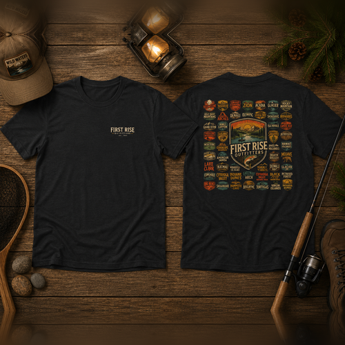National Parks fishing tee, front and back, flat-lay on weathered wood with a lantern, landing net, fly rod and boots