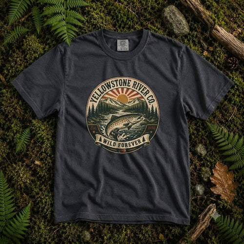 Denim Yellowstone River Co. tee laid on moss and ferns, showing a leaping trout badge with mountains and a rising sun