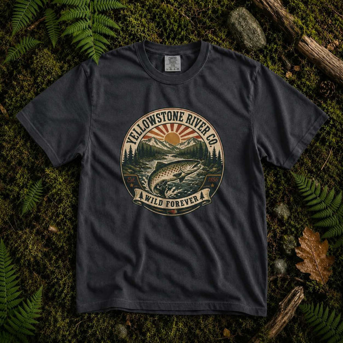Black Yellowstone River Co. trout t-shirt laid flat on a mossy forest floor with ferns, showing the Wild Forever rising sun badge