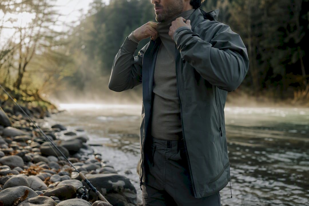Angler layering clothes at dawn riverbank