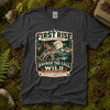 Dark heather grey Answer the Call of the Wild tee laid flat on green moss with ferns, river stones and a pinecone, showing a vintage badge of a howling wolf under a full moon