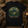 Keep It Wild Mountains tee in black, flat-lay on weathered wood with hiking boots, a lantern and a fishing rod