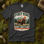 Dark heather grey Guard the Great Plains tee laid flat on green moss with ferns, river stones and a pinecone, showing a vintage badge of a bison on open grassland below snowcapped peaks — thumbnail 1