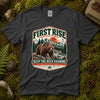 Dark heather grey Keep the Wild Roaming tee laid flat on green moss with ferns, river stones and a pinecone, showing a vintage badge of a grizzly bear above a mountain river and pines